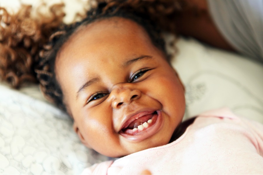 Black little girl laying down smiles brightly with her bottom baby teeth before her top teeth have erupted