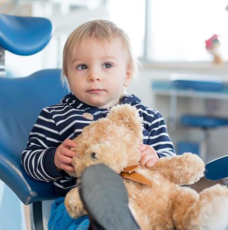little boy sitting in a dental chair, holding his teddy bear